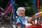 Sad, little girl in a white dress and hat, riding on a swing, summer sun and heat. playground. childhood, serenity