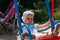 Sad, little girl in a white dress and hat, riding on a swing, summer sun and heat. playground. childhood, serenity. negative