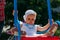 Sad, little girl in a white dress and hat, riding on a swing, summer sun and heat. playground. childhood, serenity. negative