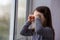 Sad lonely child girl with brown hair cries near the window. raindrops on glass. soft focus