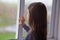 Sad lonely child girl with brown hair looks out the window. raindrops on the glass. back view