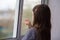 Sad lonely child girl with brown hair looks out the window. raindrops on the glass. back view