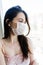 Sad lonely girl isolated at home in protective sterile medical mask on her face looking at window, bored woman because of Chinese