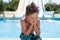 Sad lonely little boy sitting near water pool in summer resort water park