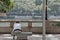 Sad lonely man sitting on a metal bench on a bridge with the river and trees in the background