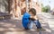 Sad, lonely, unhappy, disappointed child sitting alone on the ground. City background. Outdoor