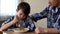 Sad male kid mixing cornflakes with spoon, father stroking child, poor appetite