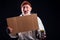 Sad man with grey beard wearing leaky gloves and warm brown hat ,holding cardboard copyspase in studio black background