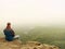 Sad man sit on the peak of sandstone rock and watching over the misty and foggy morning valley.