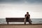 Sad man sits on an old wooden bench on the sea coast