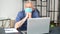 Sad mature grey-haired man wearing protective medical mask using laptop