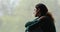 Sad melancholic young woman sitting on windowsill, watching rainy weather.