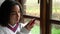 Sad mixed race African American girl teenager young woman sitting by a window using mobile cell phone during Coronavirus Pandemic