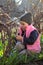 sad, offended, warmly dressed girl in a cap sits on her knees among the flowers of blue snowdrops in the vineyard