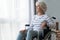 Sad paraplegic old woman sit on wheelchair look through window
