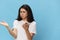 a sad, puzzled, tired woman stands with a phone in her hands spreading her arms to the sides on a light blue background