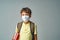 Sad schoolboy in a protective mask, standing on a gray background