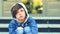 Sad schoolboy sitting on stairs outdoors. Unhappy boy in denim jacket with hood and a scraped knee. School bullying concept. Pre