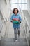 Sad schoolboy walking downstairs, carrying pile of books