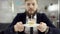 Sad serious bearded businessman, office worker is celebrating a lonely birthday in the office, he is blowing a candle on