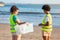 Sad serious teenager different girl and lady volunteers in vests collect garbage and bottles in box on beach