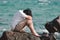 Sad stressed young Asian man hug his knee sitting on the rock of sea shore