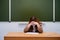 Sad teacher sits on the background of the blackboard, copy space