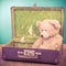 Sad Teddy Bear toy sitting in old retro suitcase front mint blue background. Vintage style photo