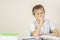 Sad tired upset schoolboy covering face with his hands sitting at table with pile of school books and notebooks at home