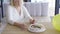 Sad unhappy mature woman sitting at the table in front of small birthday cake in emlpy room then stands up and walking