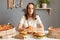 Sad unhappy woman wearing white t- shirt siting at table with fast food in kitchen looking at camera with displeased face felling