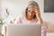 Sad upset, gray-haired, middle-aged woman is sitting in front of a laptop