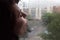 A sad woman blows air with her lips on a window fogged from the rain