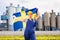 Sad woman in overalls with Sweden flag in her hands against the background of chimneys of modern factory