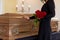 Sad woman with red roses and coffin at funeral