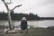 Sad woman sitting on a chair by the lake. Dark tone picture. Lonely woman