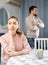 Sad woman sitting at table at home, husband quarreling with her