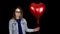 A sad woman stands with helium balls on a black background. Valentine`s Day is the day of all lovers.