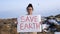 Sad woman volunteer activist stands at big landfill site with garbage with Save Earth poster demonstrates against