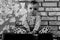 Sad about world problems small child is sitting on a iron barrel Baby boy on the background of a brick wall. Black and white