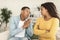 Sad young african american man asking for forgiveness from angry offended female in living room interior