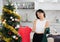 Sad young Asian girl trying to choose a dress standing next to Xmas tree