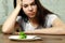 Sad young brunette woman dealing with anorexia nervosa or bulimia having small green vegetable on plate. Dieting problems, eating