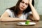 Sad young brunette woman dealing with anorexia nervosa or bulimia having small green vegetable on plate. Dieting problems, eating