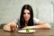 Sad young brunette woman dealing with anorexia nervosa or bulimia having small green vegetable on plate. Dieting problems, eating