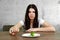 Sad young brunette woman dealing with anorexia nervosa or bulimia having small green vegetable on plate. Dieting problems, eating