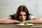 Sad young brunette woman dealing with anorexia nervosa or bulimia having small green vegetable on plate. Dieting problems, eating