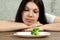 Sad young brunette woman dealing with anorexia nervosa or bulimia having small green vegetable on plate. Dieting problems, eating