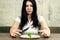 Sad young brunette woman dealing with anorexia nervosa or bulimia having small green vegetable on plate. Dieting problems, eating