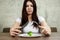 Sad young brunette woman dealing with anorexia nervosa or bulimia having small green vegetable on plate. Dieting problems, eating